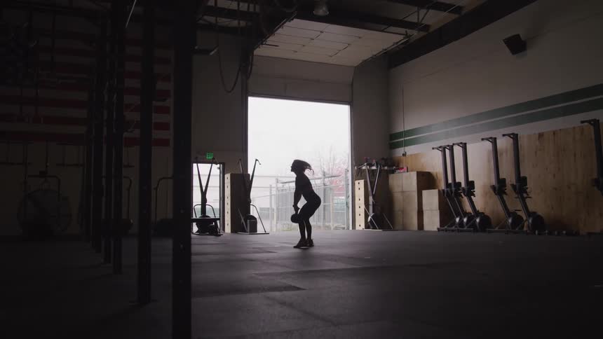 Woman exercising with a kettlebell in a gym with natural light coming from a large open door in the background