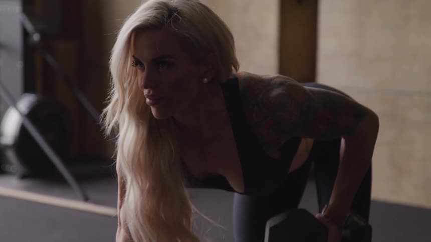 Blonde woman doing triceps workout with dumbbell in a gym