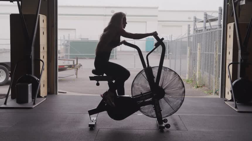 A blonde woman rides a large stationary bicycle inside a garage