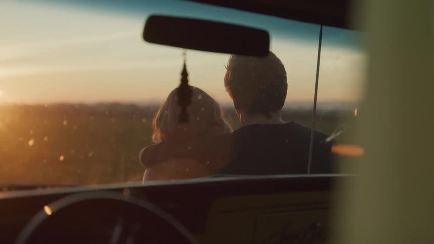 A man and woman are standing outside a vehicle watching the sun rise