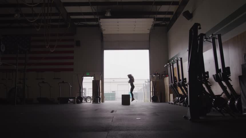 A woman is working out by jumping on and off a box in a gym