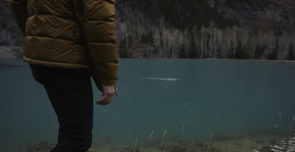 A man throwing rocks across some water making it skip