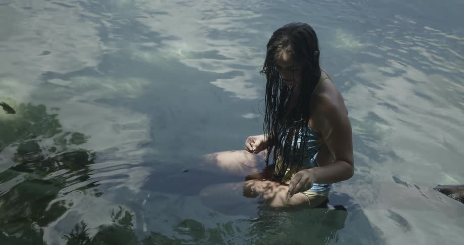 A woman sits on a floating tree trunk in a lake