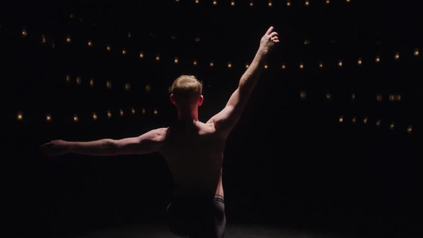 A male ballet dancer is dancing on a stage