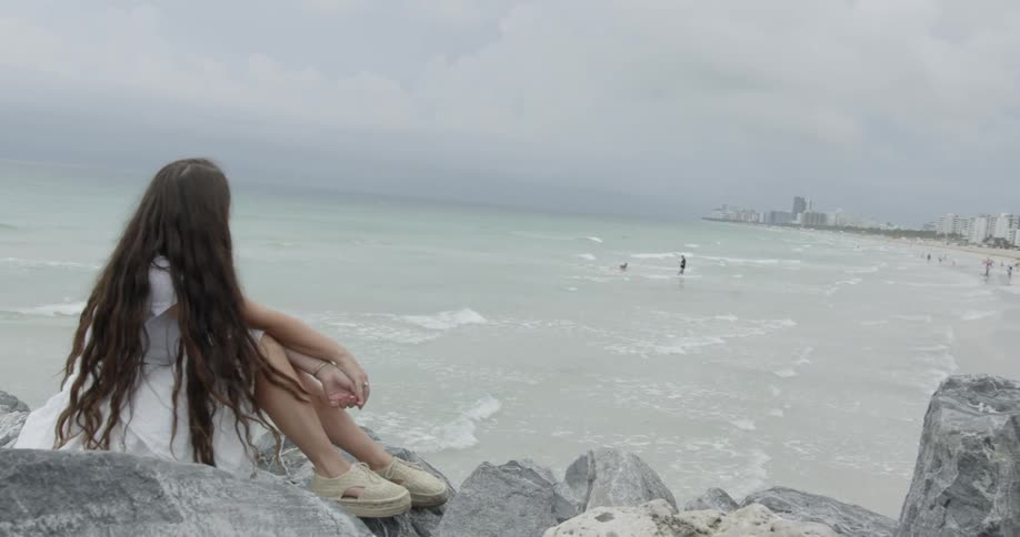 A woman sits on some rocks by the rough shore