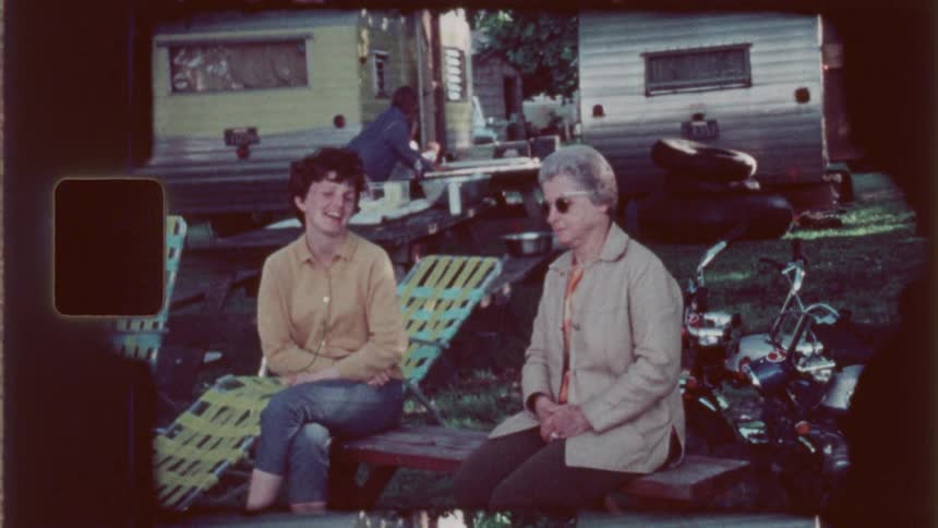 Two women one of them a lady with sunglasses sitting on a chair outdoors