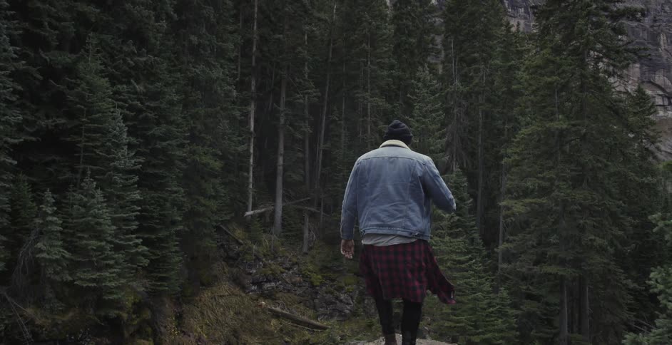 Person in hat and jean jacket hike through forest