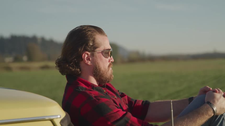 A man is looking over the field while sitting by his car