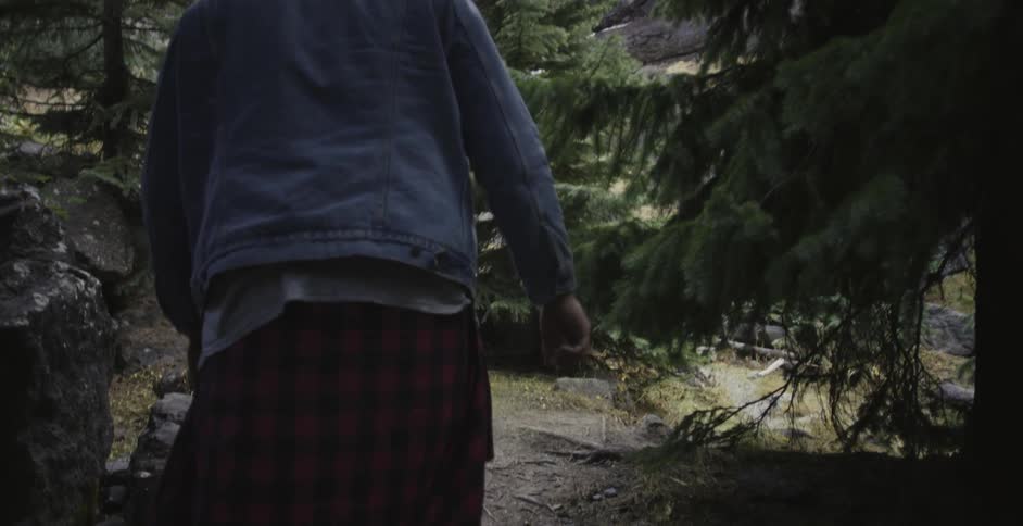 A man wearing a denim jacket walks in the woods
