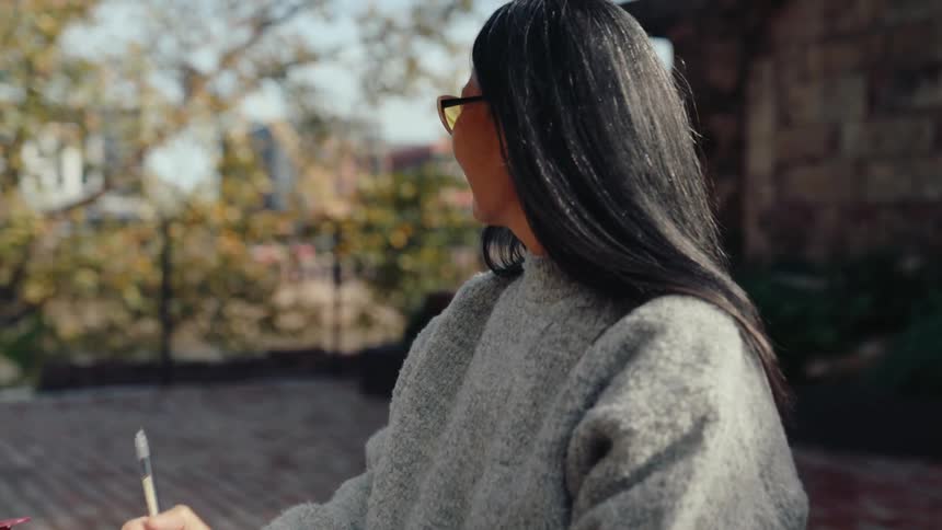 A clip of an asian lady sitting outdoor and writing in her diary