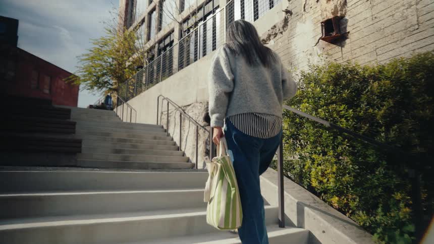 Woman with a bag walking up the stairs outdoors in a city
