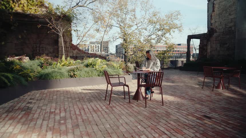 Woman sitting at a table in an outdoor cafe writing in a book