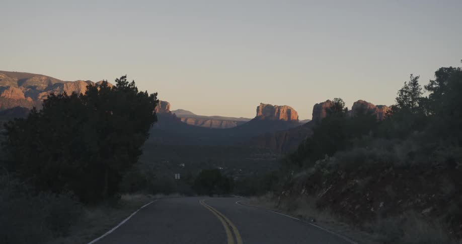 Sun setting on some rocky mountains as seen from a two lane roadway
