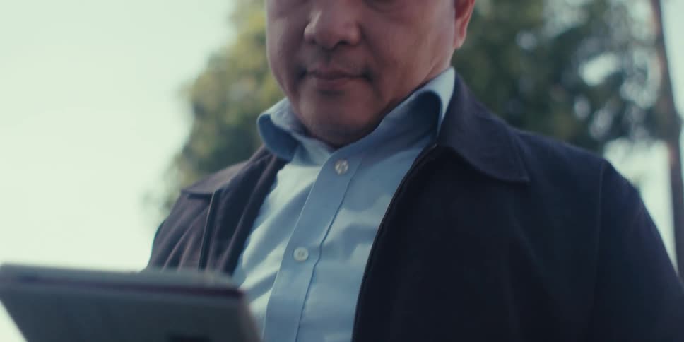 A person sits on a bench in a residential neighborhood writing on a tablet with a stylus