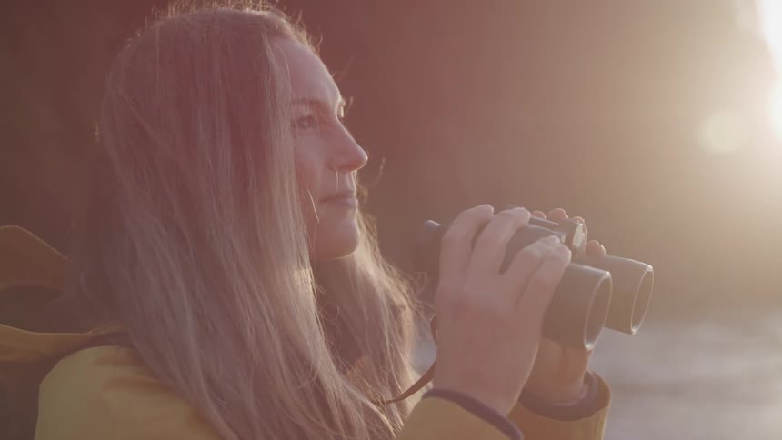 A woman is using her binoculars on the beach