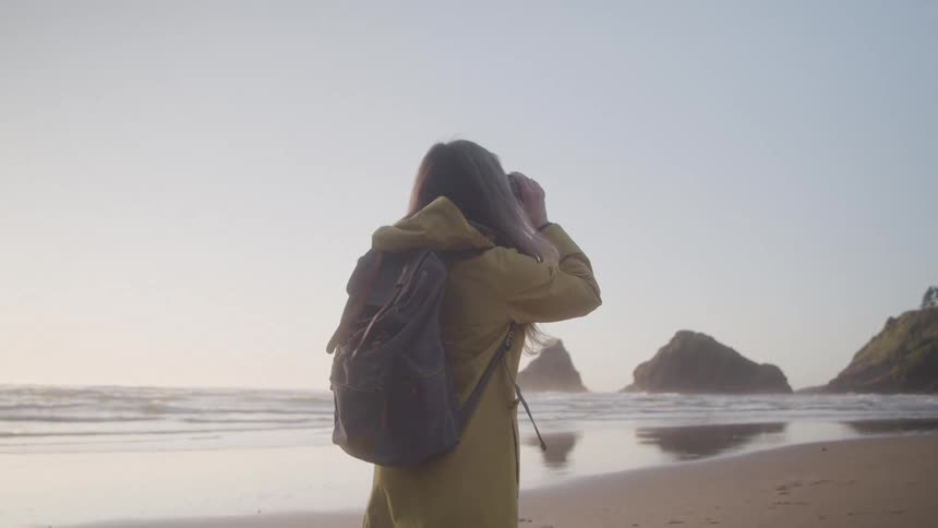 Woman with binoculars looking while standing on a beach at dawn