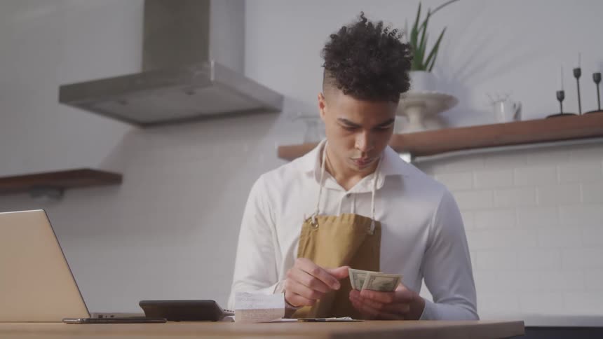 A man is counting money in the kitchen