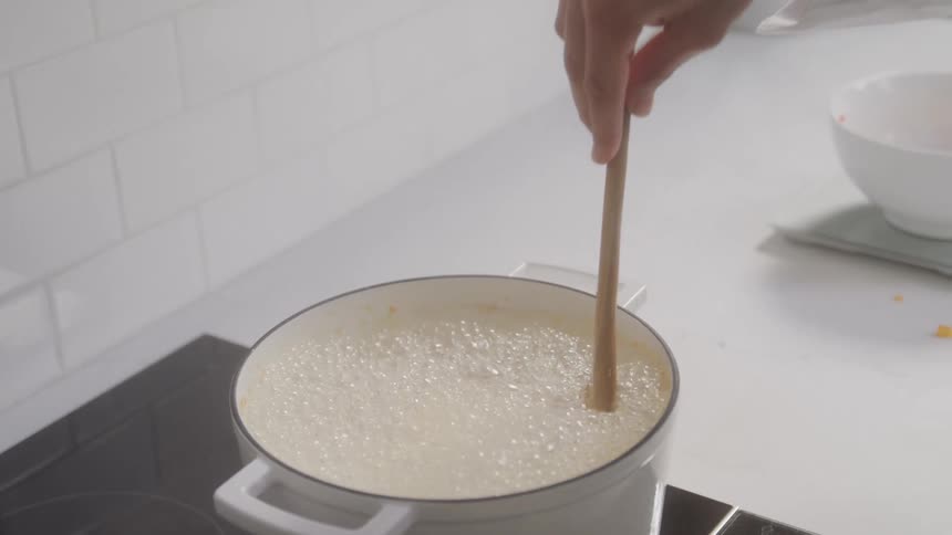 A person is stirring a pot of soup with a wooden spoon