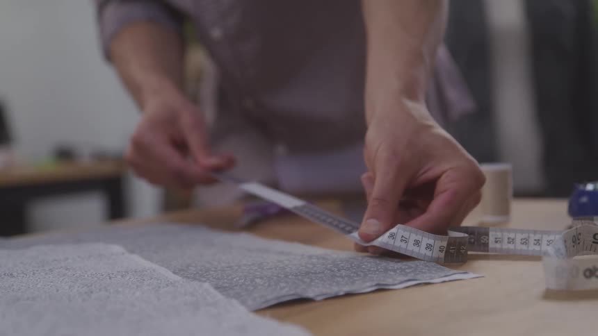 A man is using a measuring tape to measure something on a table