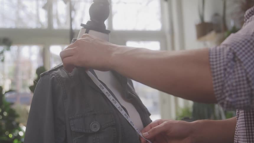 Pair of hands with a tape measuring a garment on a mannequin