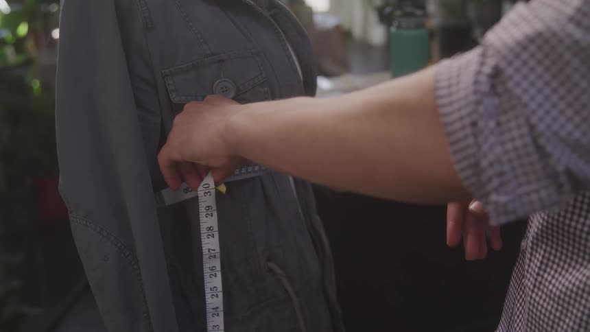 Close up view highlights hands using a measuring tape to precisely measure the side of a jacket that is draped on a mannequin