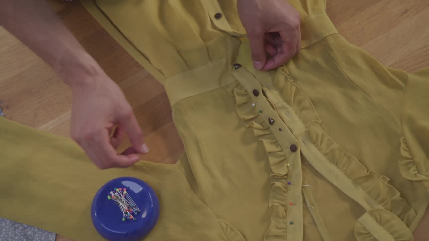 Pair of hands of a seamstress putting buttons on a womens jumpsuit on the table