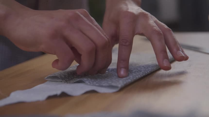 Pair of hands with a needle working with a fabric on top of a wooden table