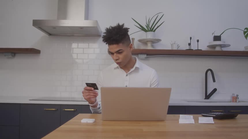 Young man sitting in front of an open laptop and holding a credit card