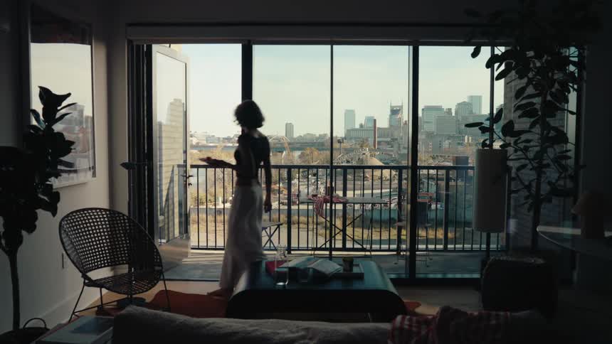 Woman carries a plate onto the balcony and sits at a table on an autumn day