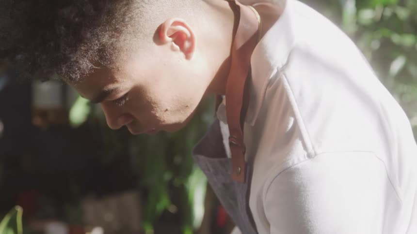 The sun reflects off a man as he looks down surrounded by plants