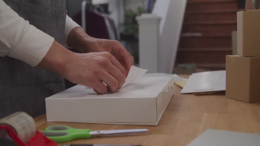 A persons hand sticking a paper onto the surface of a small white box that is on a wooden table