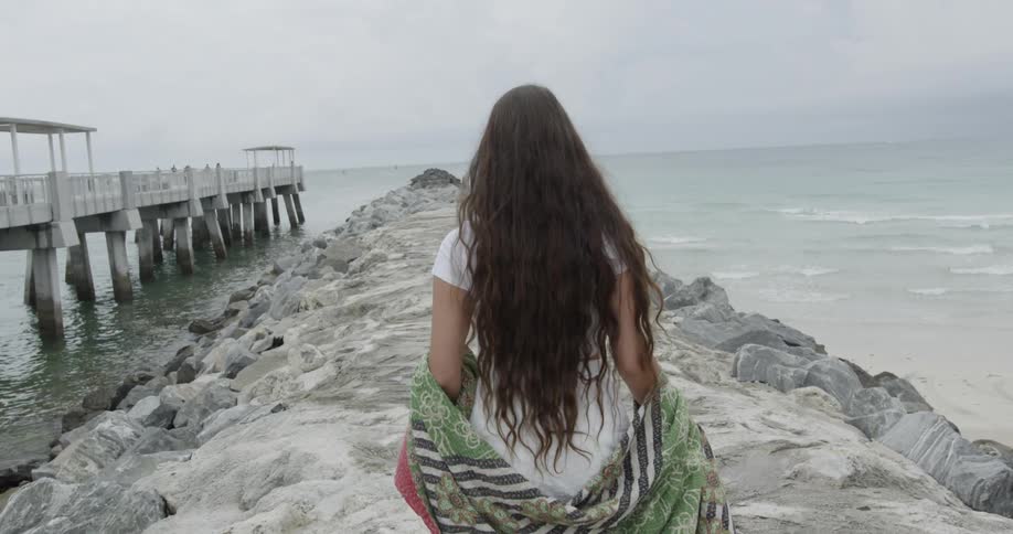 Long-haired woman walking on a rock formation dividing the sea