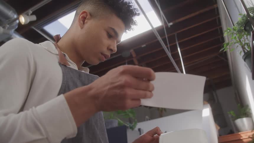 A man wearing an apron is in a greenhouse peeling a sticker from paper