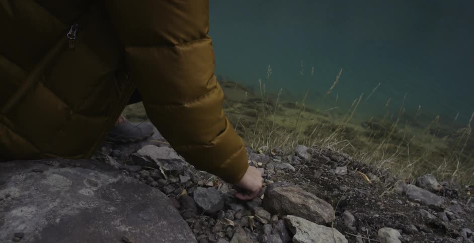 Person kneeling down by water and looking through rocks