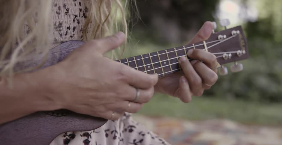A woman is sitting and playing a ukulele during daylight