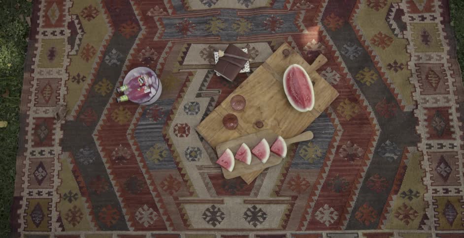 Watermelon, drinks and a book sitting on a picnic blanket