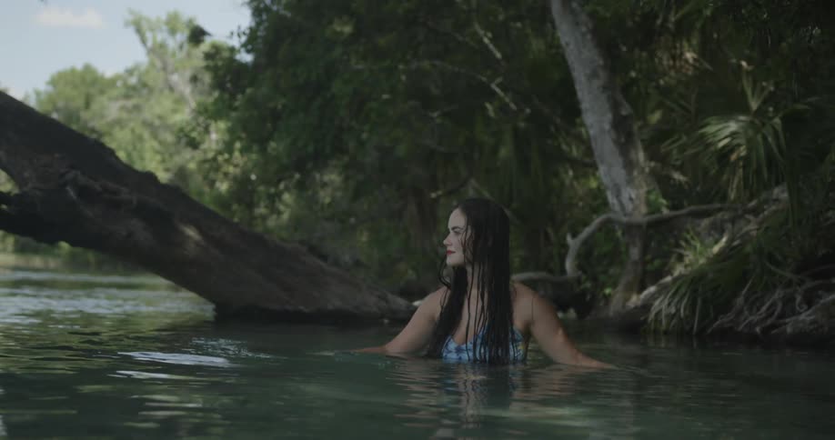 A woman is sitting in shallow water near the shore during day