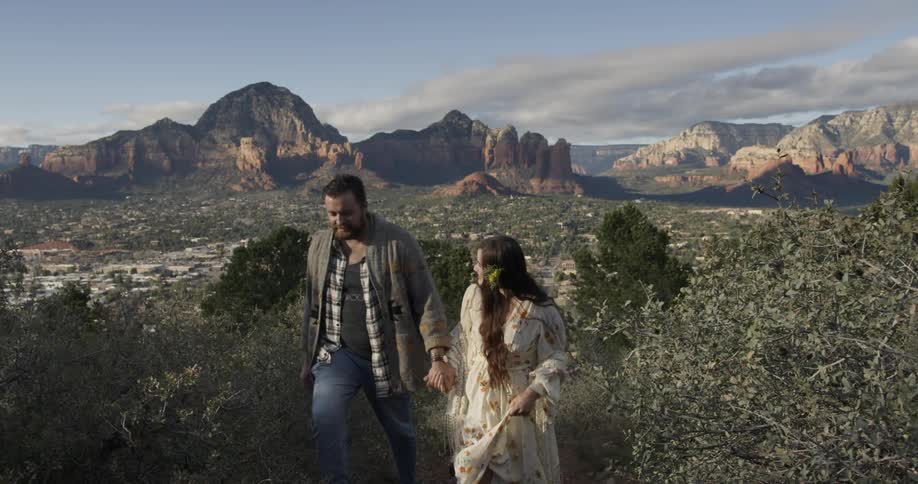 Man and woman in white dress walking through shrubbery in wilderness