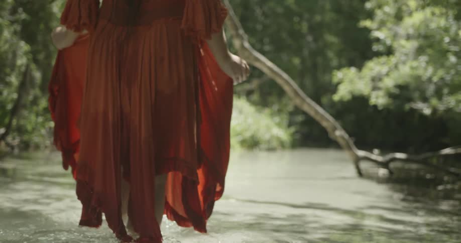 A woman is holding her dress up as she wades in water