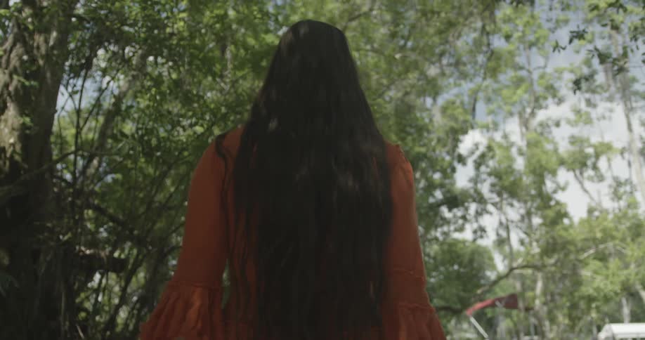 A woman is walking beneath tall trees on a sunny day