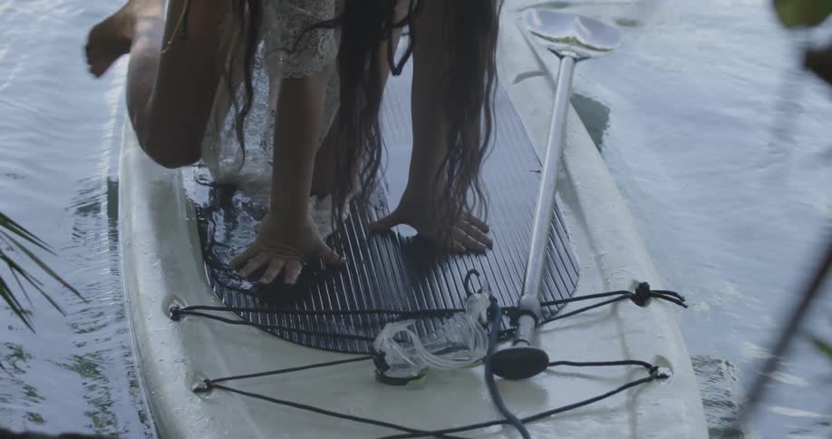 Long-haired woman getting off of her floating surfboard like board in shallow water