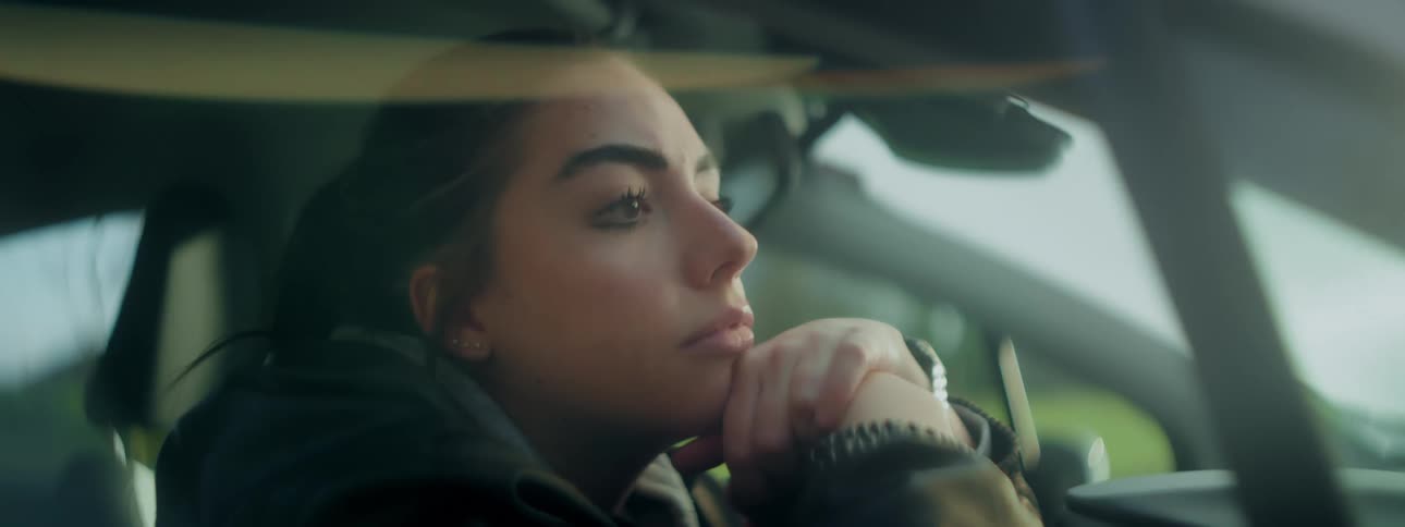 Woman rests her chin on her hand while staring out of a car window