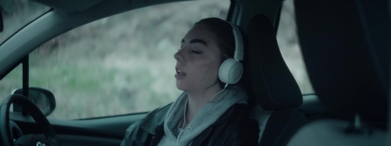 Woman sits in her parked car singing while listening to music on her headphones