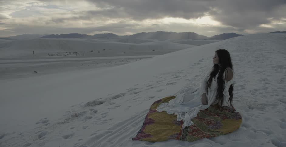 Woman in white dress sitting in snow covered wilderness