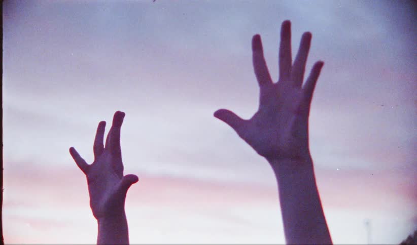 Two hands are raised against a colorful sunset sky