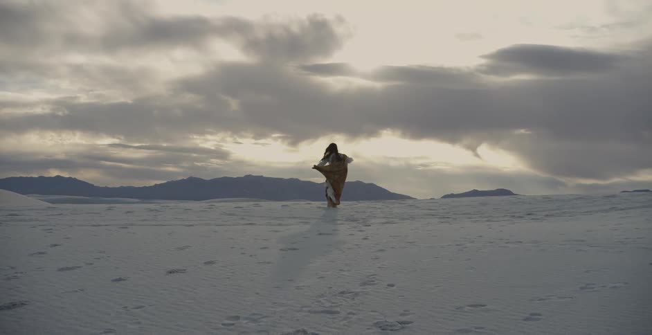 Woman in white dress spinning around in the sand