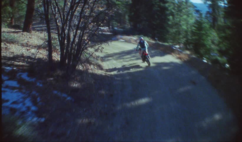A motorcyclist rides along a winding dirt road through a forest