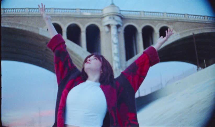 Woman outdoors next to an overpass putting her hands up