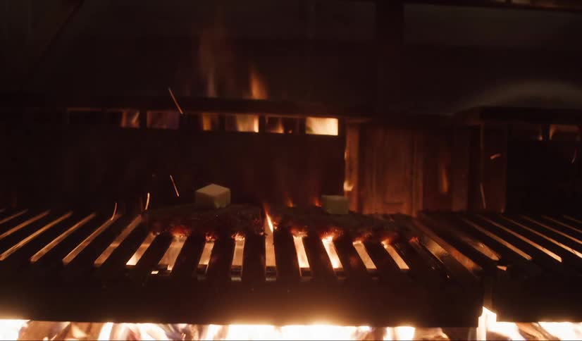 Hand placing cheese cubes on top of slices of meat being cooked on the grill
