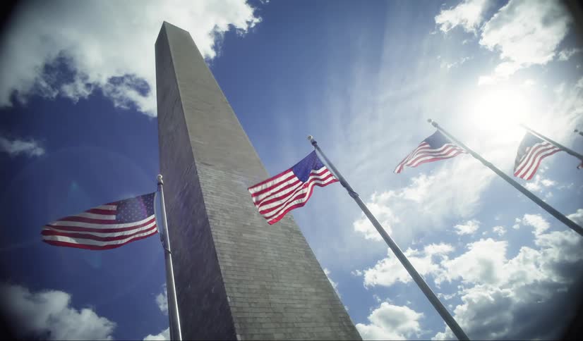 Washington monument with american flags around it under a clear sunny sky